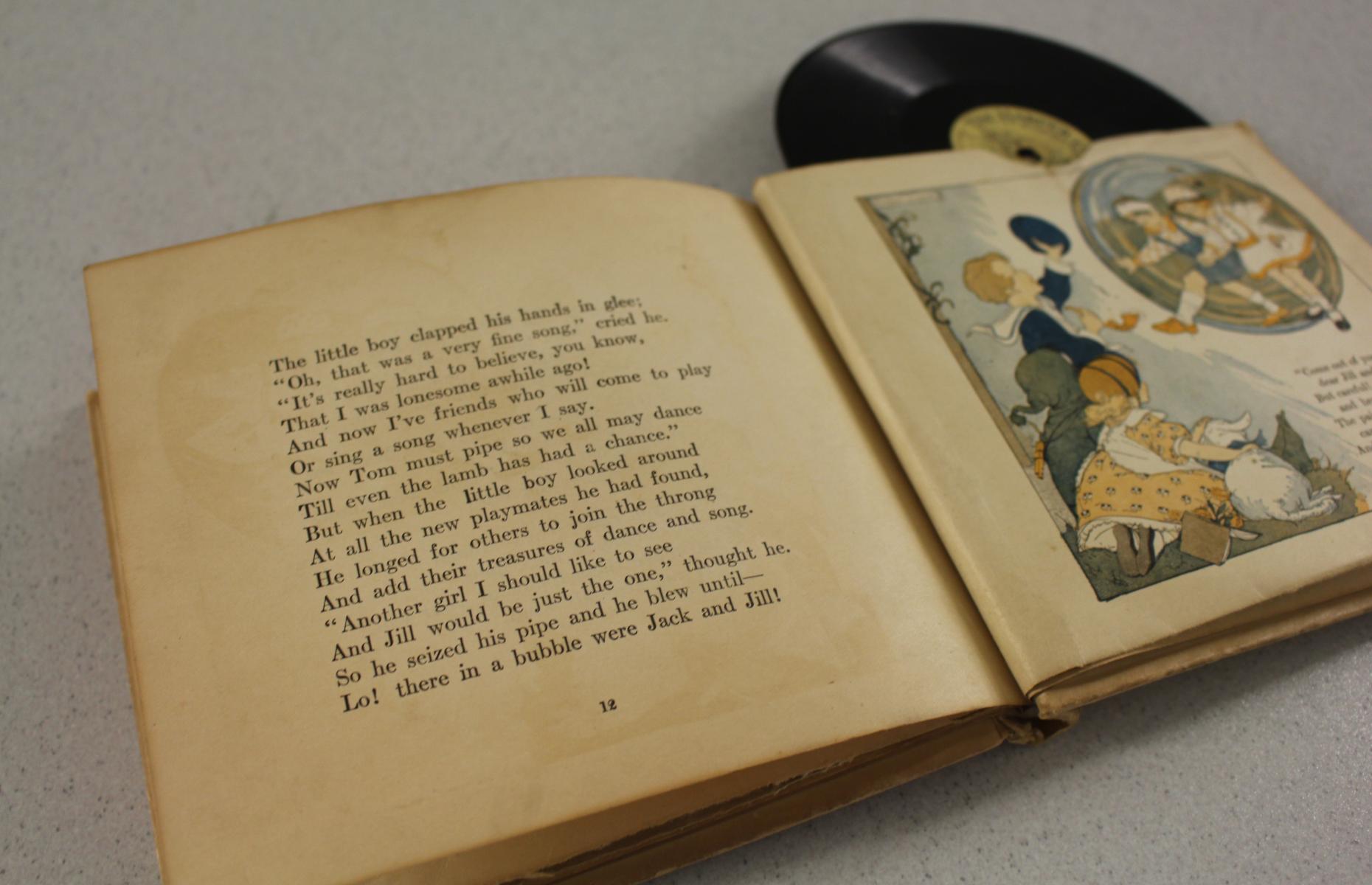 Eine Nahaufnahme von einer Doppelseite im Buch. Auf der ersten Seite ist Text und auf der zweiten Seite befindet sich eine Illustration. Oben lugt eine Schelllackplatte heraus.