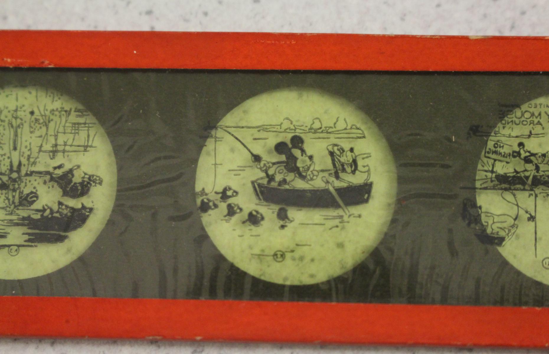 Nahaufnahme einer der Mickey Mouse Glasdurchziehbilder. Die Szene zeigt Mickey und Pluto auf einem Boot beim Angeln.