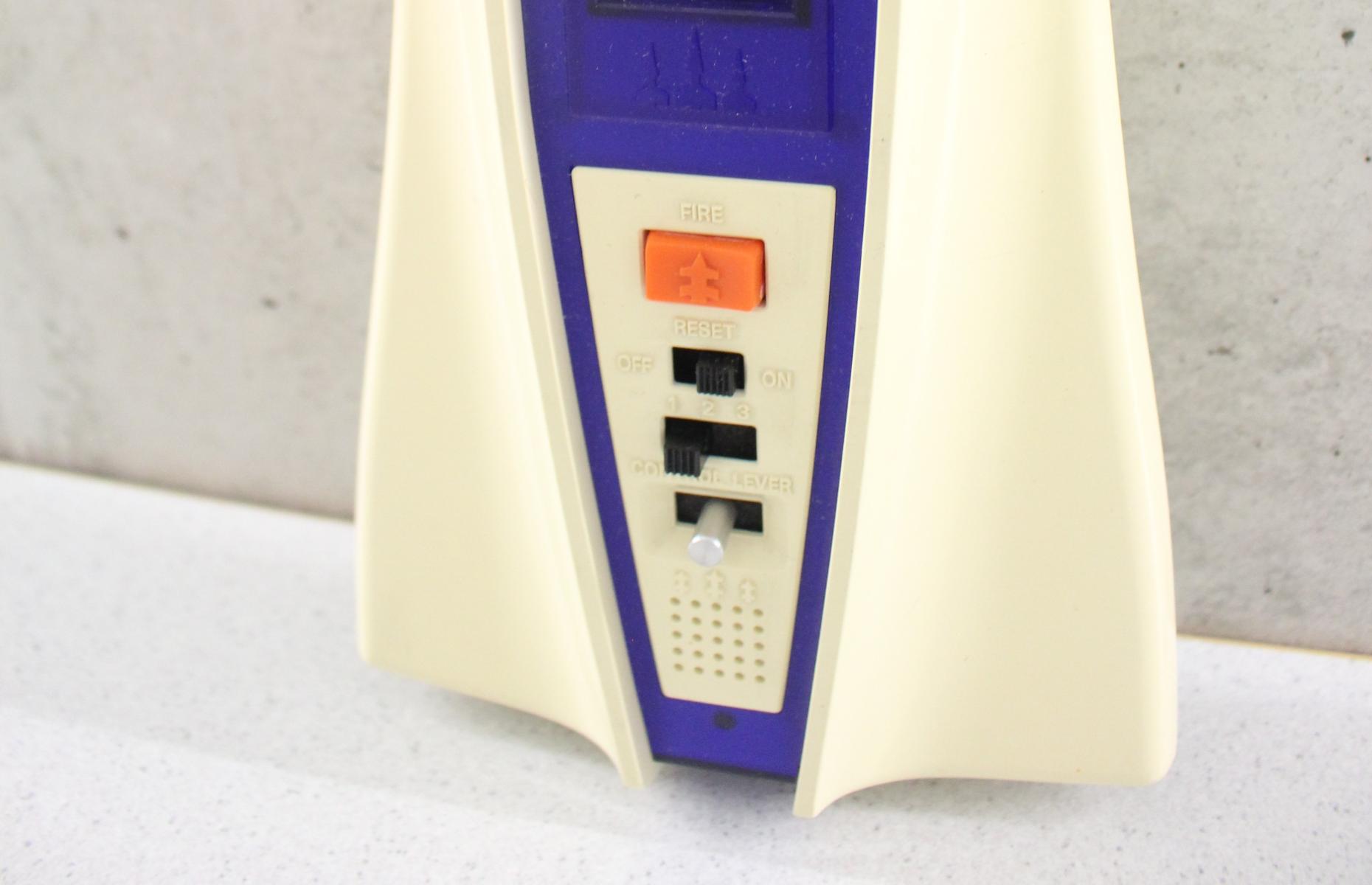 Hier ist der untere Teil des Ufo Master Blasters in weiß, mit einem blauen Mittelteil und Bildschirm zu sehen. Der Hauptsteuerknopf ist orange